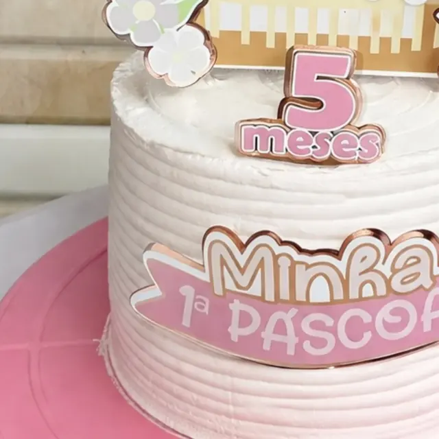 Detalhe de bolo rosa e rose gold com topo “Minha 1ª Páscoa” e “5 meses”
